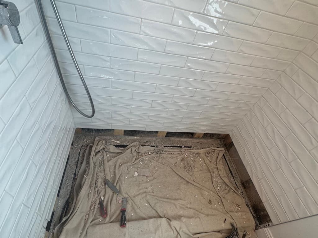 Shower opened at base to expose damaged lower wall and framing